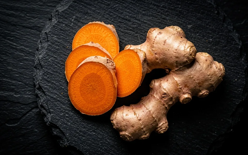 Fresh turmeric and ginger roots on a dark cutting board